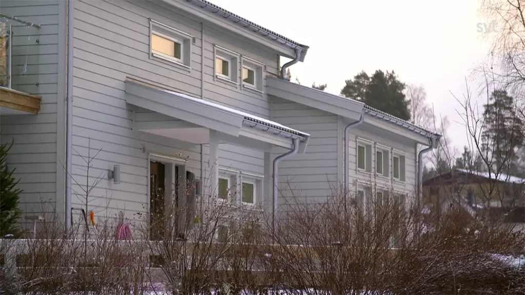 Stiligt - Ett modernt grått hus i två våningar med vita detaljer, sett en vinterdag med kala buskar och snöfläckar på gården.