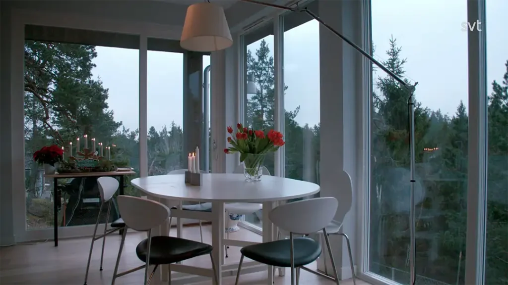 Stiligt - En modern matplats med ett runt vitt bord, svarta och vita stolar, en vas med röda tulpaner och fönster från golv till tak med utsikt över träd. Ljus och dekorationer sitter på ett sidobord.
