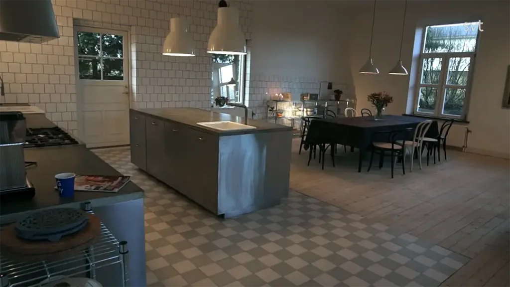 Stiligt - Ett rymligt kök med en central ö, vitvaror i rostfritt stål, klinkergolv, ett matbord med stolar och stora fönster som släpper in dagsljus.