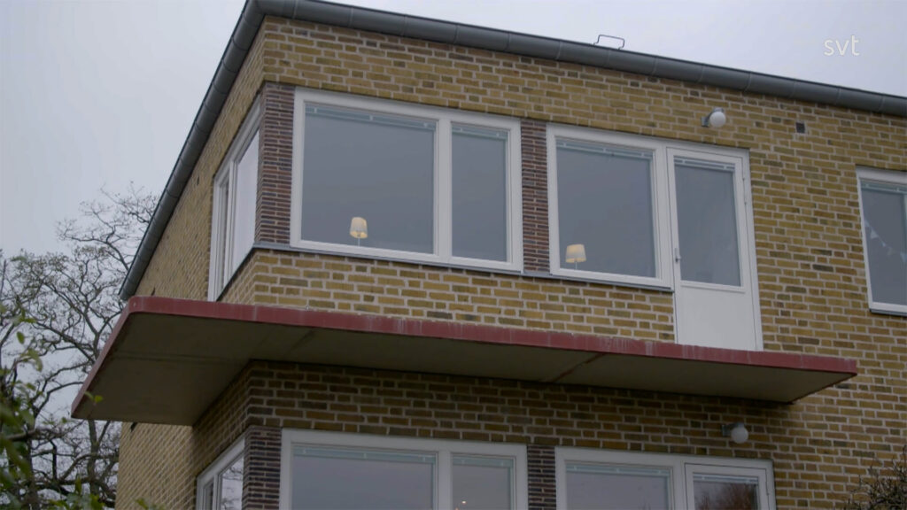 Stiligt - En tvåvånings tegelbyggnad med stora fönster och ett platt överhängande tak, sett underifrån en molnig dag.