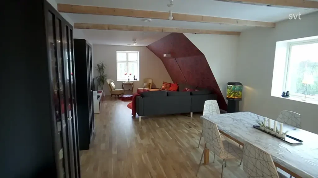 Stiligt - Vardagsrum och matplats i öppen planlösning med trägolv, en grå soffa, röda detaljer, ett akvarium och stora fönster som släpper in naturligt ljus.