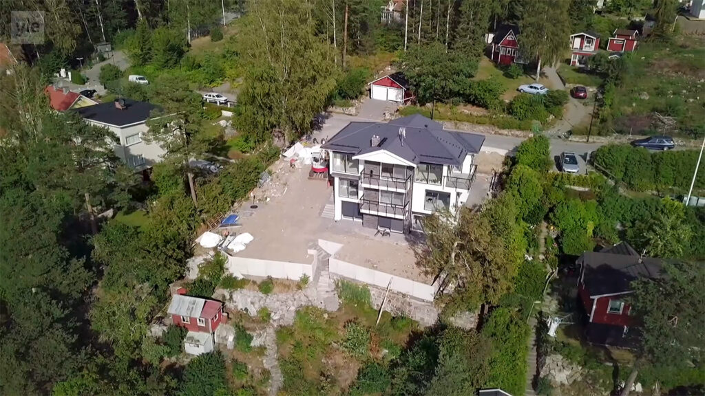 Stiligt - Flygfoto över ett stort modernt hus med grått tak omgivet av träd och andra mindre byggnader i ett frodigt, grönt kvarter.