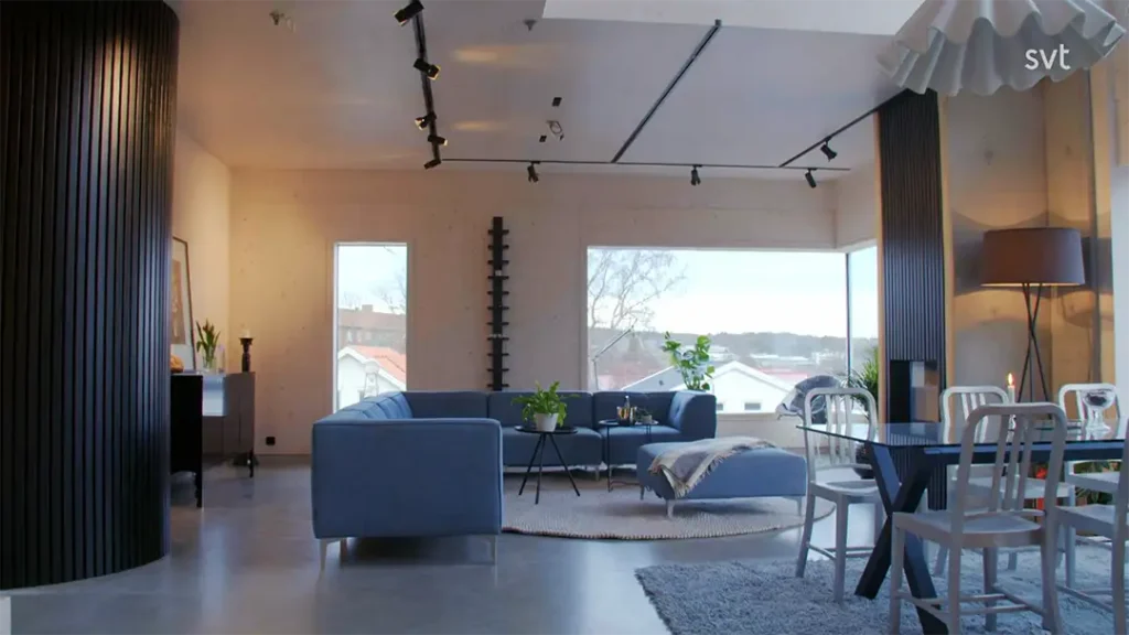 Stiligt - Modernt vardagsrum och matplats med stora fönster, blå soffa, rund matta, matbord med stolar, golvlampa och minimalistisk inredning.