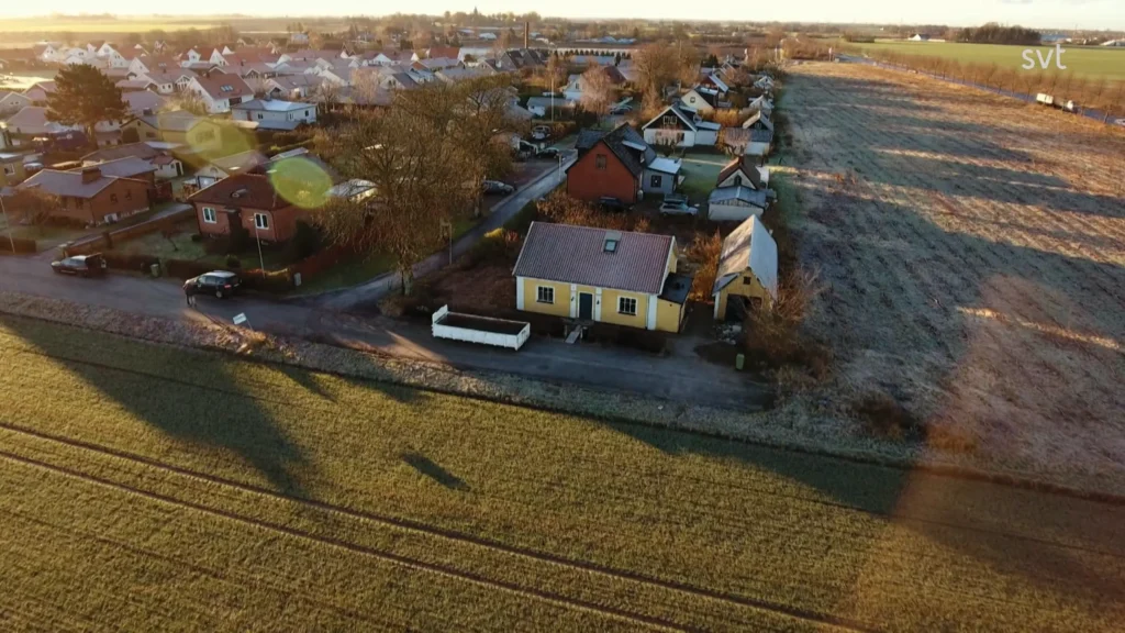 Stiligt - Flygfoto över ett förortsområde med hus, ett frostigt fält och långa morgonskuggor under klar himmel.