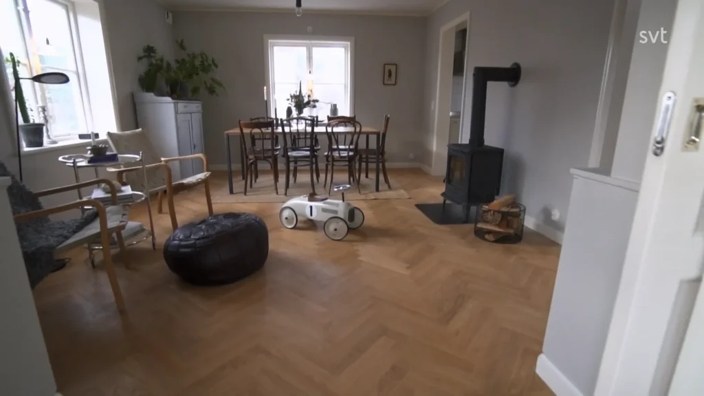 Stiligt - En matplats med ett träbord och stolar, en svart vedspis, en leksaksbil, en rund ottoman och en växt i hörnet, med naturligt ljus från ett fönster.