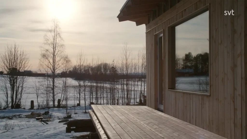 Stiligt - En träbyggnad med ett däck har utsikt över ett snölandskap med kala träd under en ljus, låg sol. Bokstäverna "svt" visas i det övre högra hörnet.