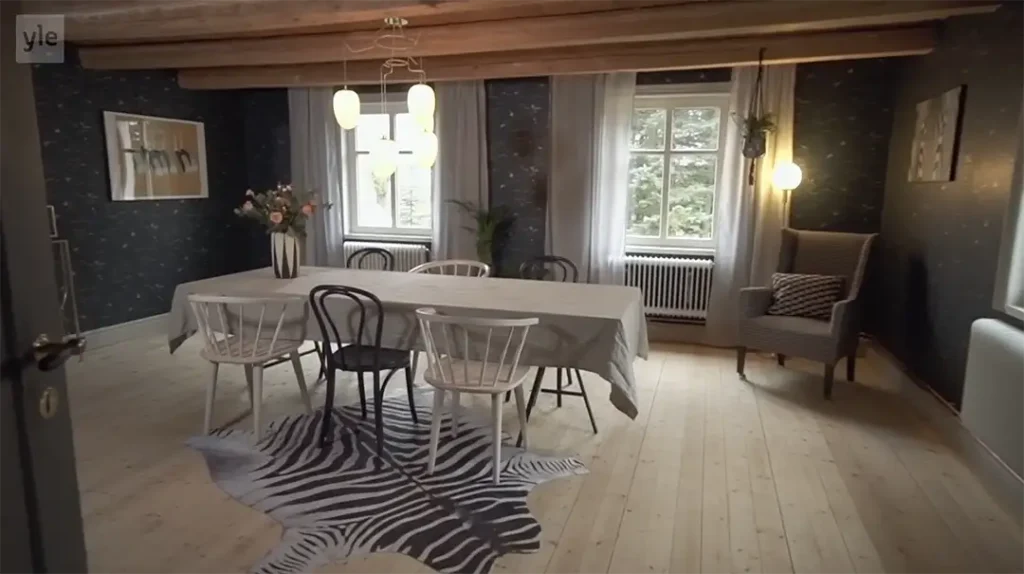 Stiligt - En matsal med ett bord täckt av en grå duk, stolar som inte matchar varandra, en zebramönstrad matta och stora fönster som släpper in naturligt ljus.