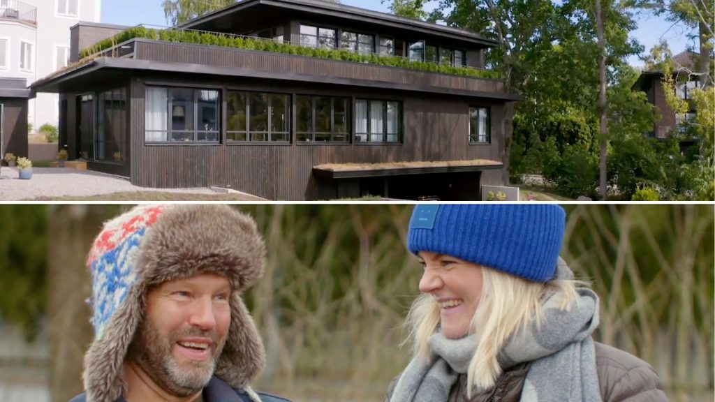 Stiligt - Ett modernt mörkt trähus med stora fönster; nedanför, en man i en lurvig hatt och en kvinna i en blå mössa som ler utomhus.