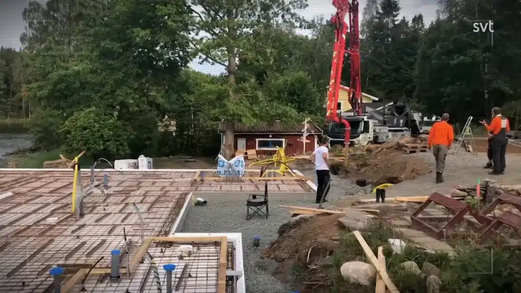 Stiligt - Byggarbetsplats med armeringsjärn på plats, arbetare närvarande, utrustning och material utspridda och träd i bakgrunden.