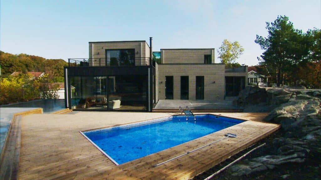 Stiligt - Modernt tvåvåningshus med stora fönster, omgivet av ett trädäck, med en rektangulär utomhuspool delvis fylld med löv.