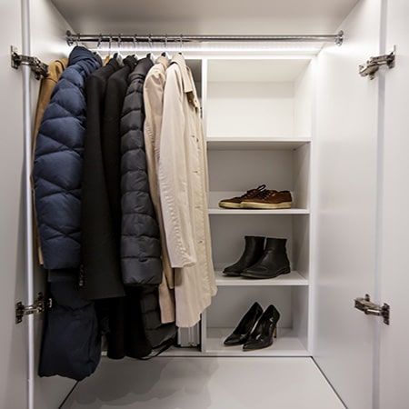 Stiligt - Öppen vit garderob med flera rockar hängande på en stång och flera par skor placerade på hyllor till höger.