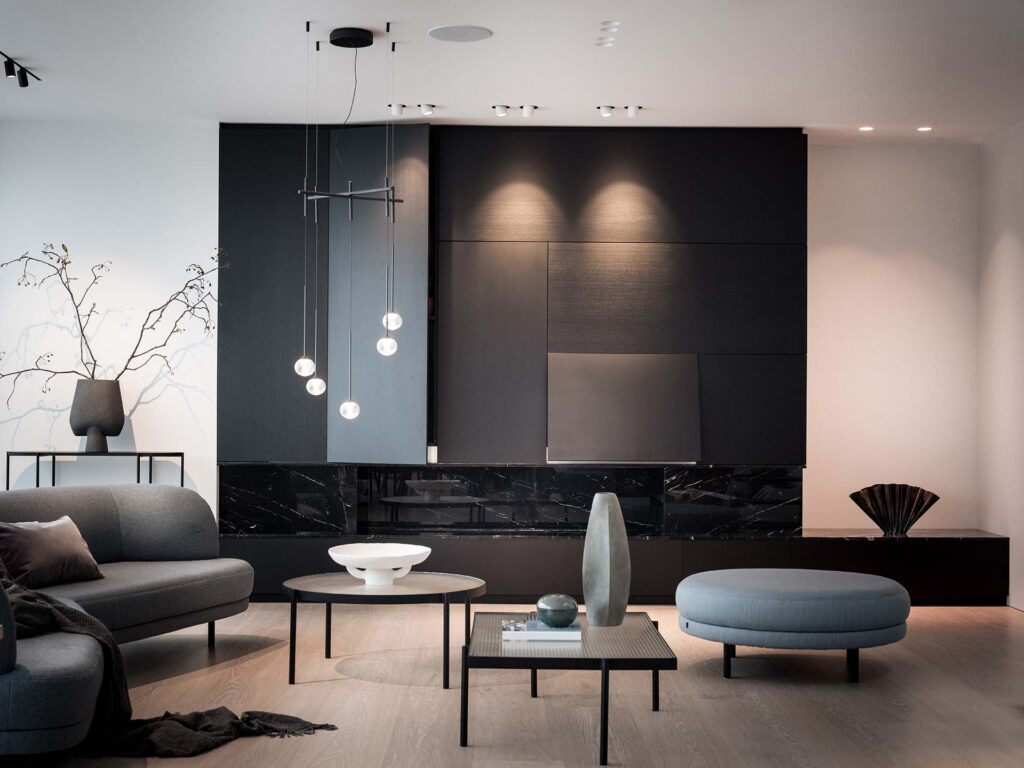 Stiligt - Modernt vardagsrum med minimalistisk svart accentvägg, grå soffa, rund ottoman, taklampor i glas och enkla dekorativa föremål på bord.