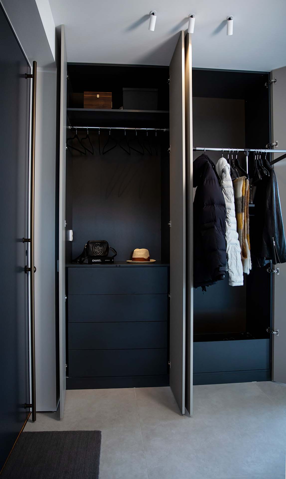 Stiligt - Öppen modern garderob med hängande svarta galgar, några jackor och halsdukar, några lådor på översta hyllan, en hatt och en väska på mittenhyllan, med stängda lådor under.