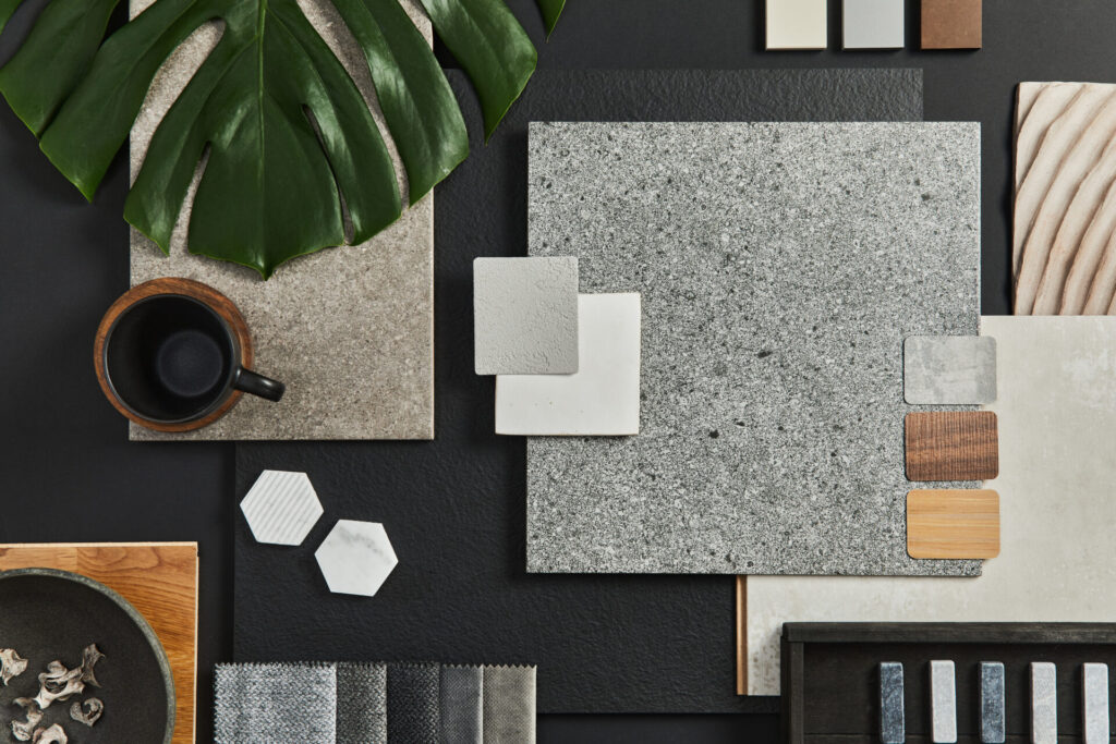 Stiligt - Blandade materialprover, kakel, tygprover, en kopp kaffe och ett stort grönt blad arrangerat på en mörk yta.