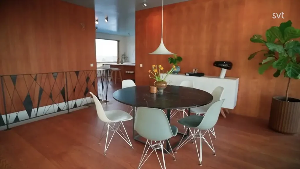 Stiligt - Modern matplats med ett runt svart bord, fem vita stolar, en hänglampa, en skänk, en krukväxt och träpaneler på väggar.