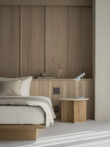 Stiligt - Minimalistiskt sovrum med en neutral färgpalett, med en säng, ett nattduksbord i trä med en lampa och en liten vas med torkade blommor mot en vägg med träpanel.