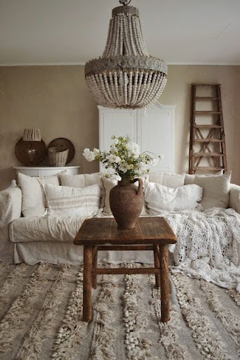 Stiligt - Ett rustikt vardagsrum med en vit soffa, texturerad filt, träbord med en vas med blommor, pärlkrona och en trästege mot väggen.