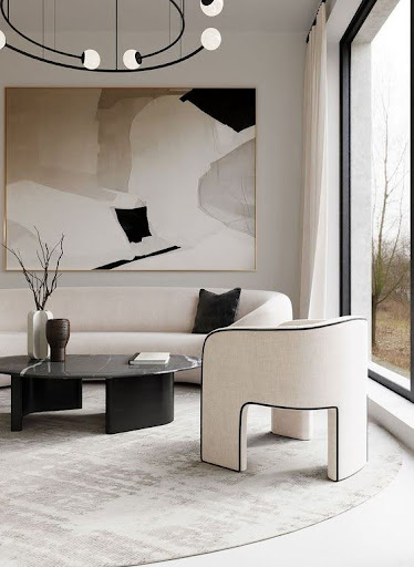 Stiligt - Minimalistiskt vardagsrum med en svängd vit soffa, modern fåtölj, svart soffbord, abstrakt väggkonst, stort fönster och neutral färgpalett.