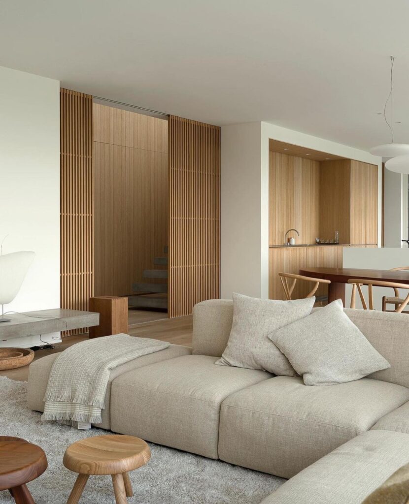 Stiligt - Ett modernt vardagsrum med en beige soffa, träpallar, en liten matplats och träribbor, med neutrala färger och minimalistisk inredning.
