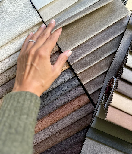 Stiligt - En hand vidrör tygprover arrangerade i en gradient från ljusa till mörka neutrala toner.