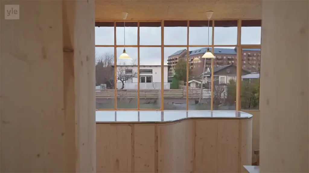 Stiligt - Interiörvy av ett trärum med stora fönster med utsikt över bostadshus och träd, med tre taklampor hängande ovanför en disk.