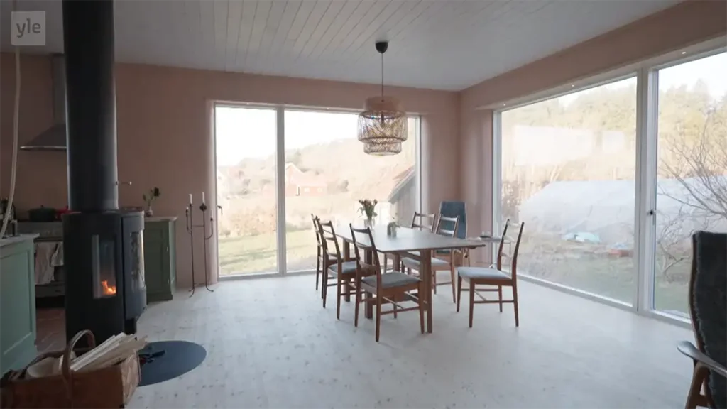 Stiligt - En matplats med ett träbord, sex stolar, en öppen spis och stora fönster som visar ett utomhuslandskap.