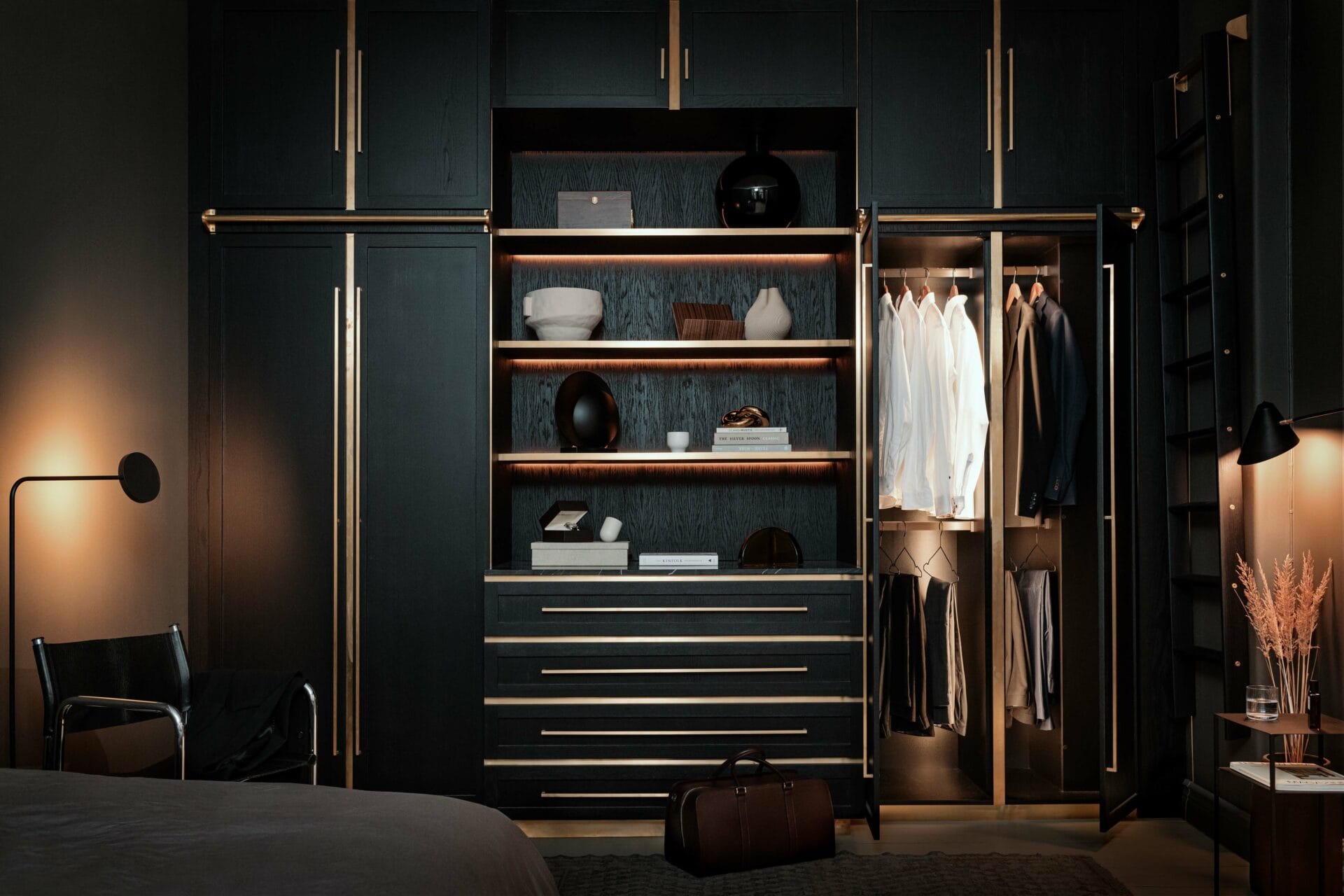 Stiligt - En modern, mörkfärgad garderob med öppna hyllor och hängande kläder, upplyst av inbyggd belysning, i en elegant sovrumsmiljö.