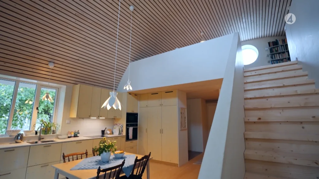 Stiligt - Modernt kök med ljusa träskåp, ett matbord och trappor som leder till en övre våning; lamelltak och naturligt ljus från fönster.