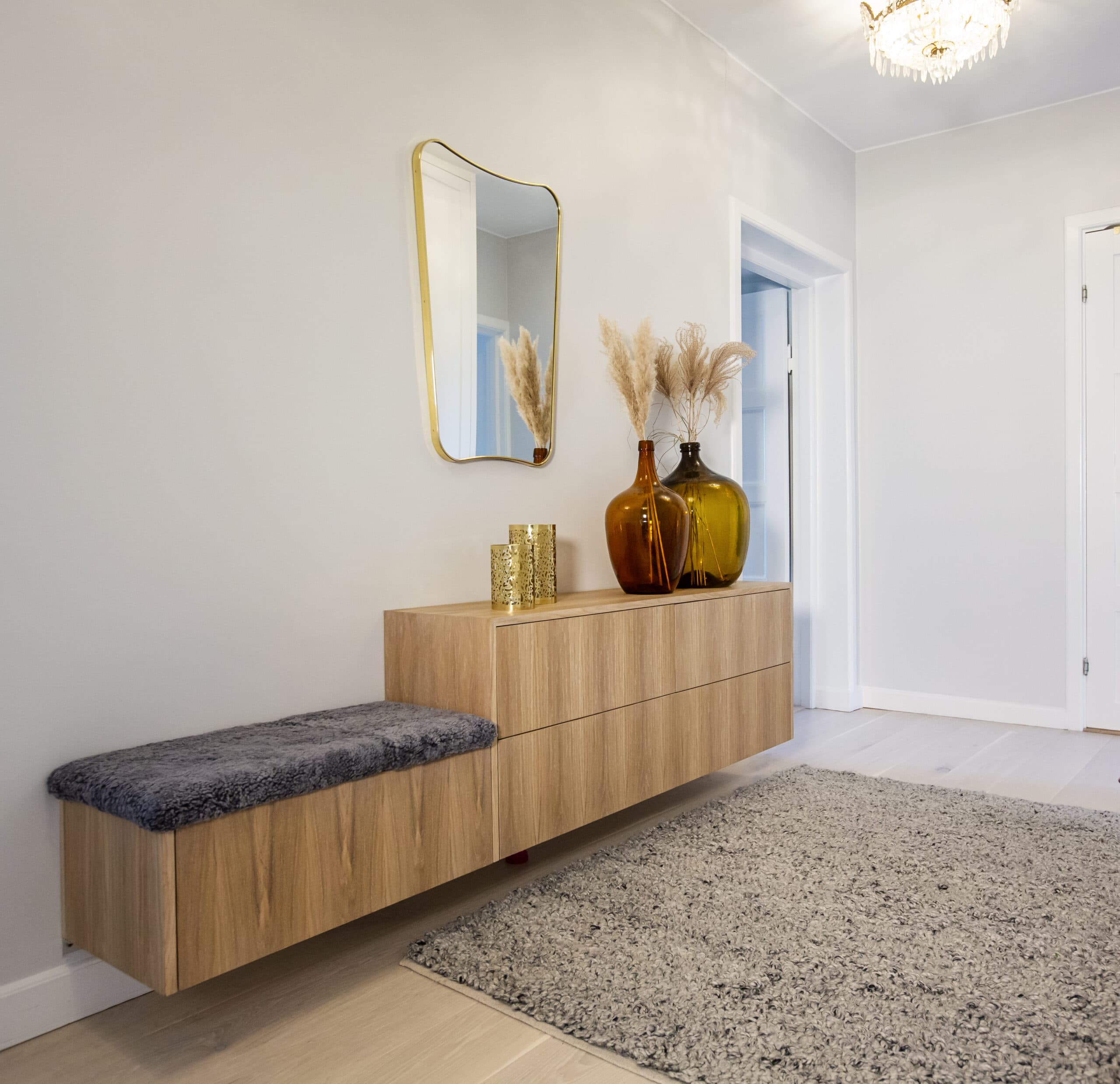 Stiligt - En modern hall med en flytande träkonsol, en grå vadderade bänk, dekorativa vaser, en spegel och en grå strukturerad matta på ett ljust golv.