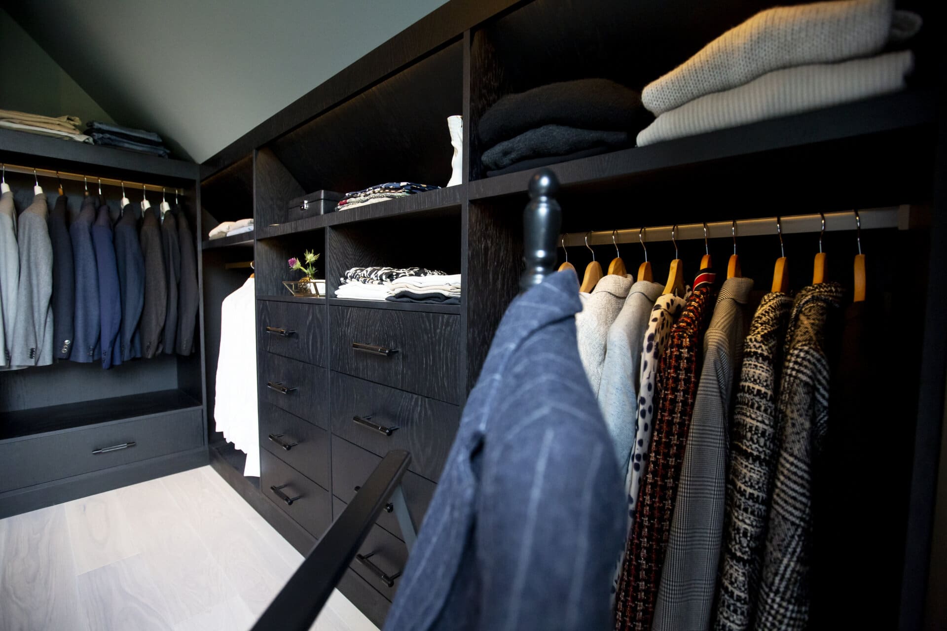 Stiligt - Svart Walk in closet En stiligt organiserad klädkammare med svarta hyllor, med hängande jackor och tröjor, vikta kläder och några lådor.