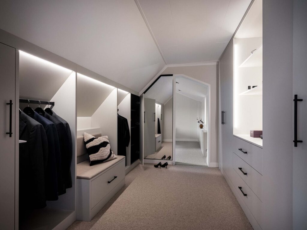 Stiligt - Modernt ljus walk in closet med inbyggda garderober, hängdräkter, dämpad bänk, öppna hyllor och en stor golvspegel i slutet.