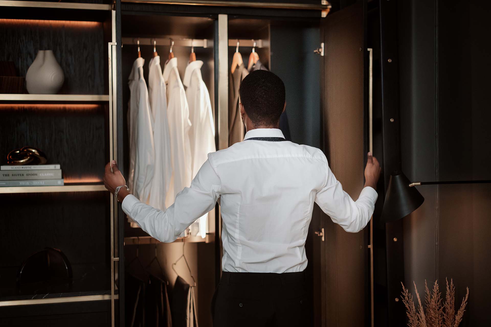 Stiligt - En person i en vit skjorta öppnar en garderob och tittar på flera vita skjortor som hänger inuti.