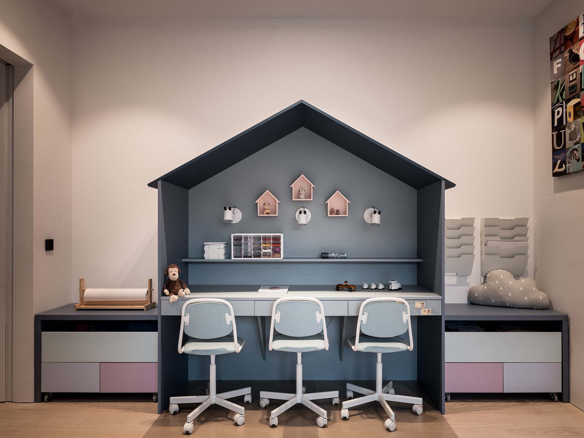 Stiligt - Barns studieområde med tre blå stolar vid ett skrivbord, husformade hyllor, väggmonterad dekor, förvaringslådor och en uppstoppad björn.