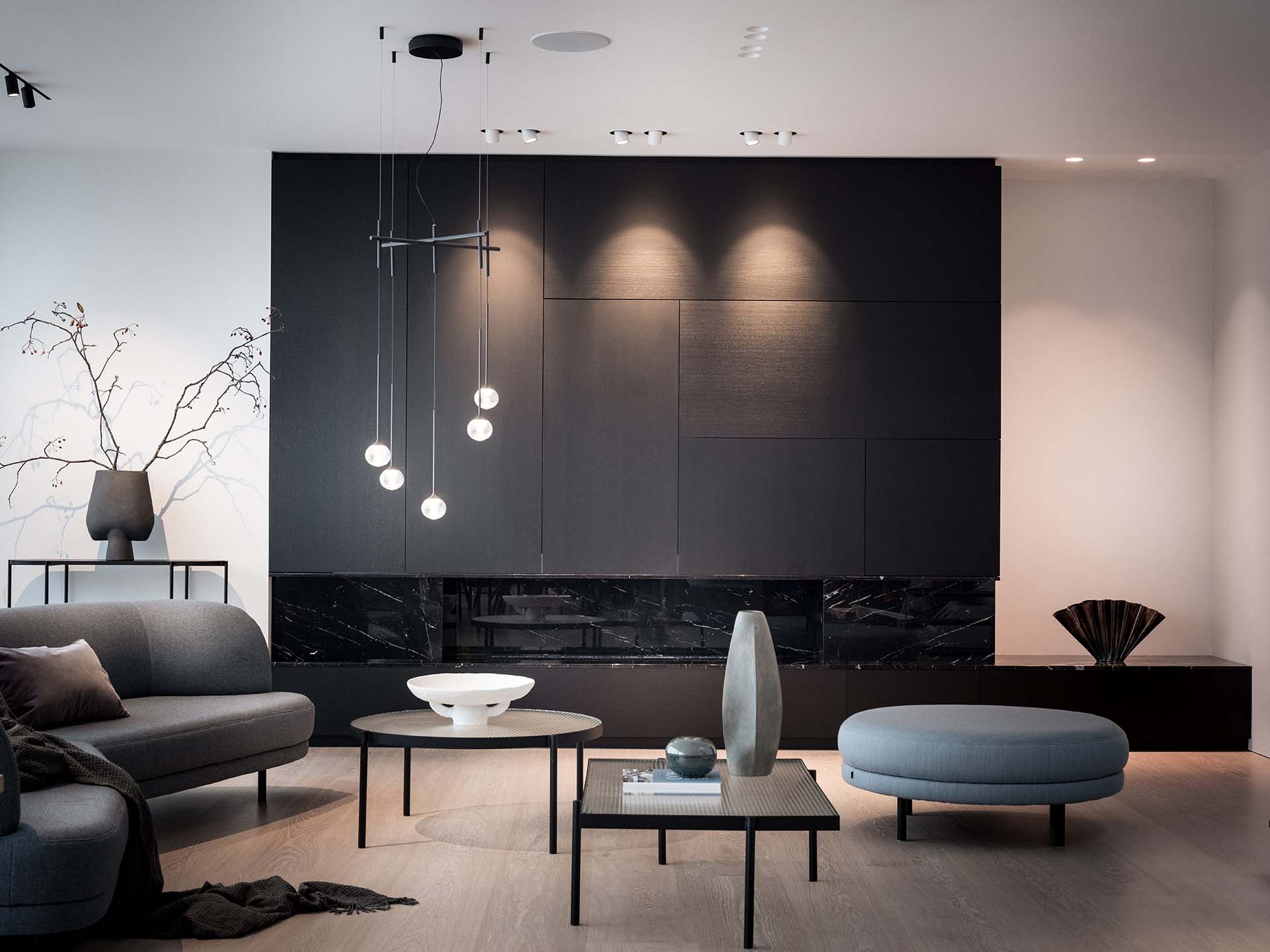 Stiligt - Modernt vardagsrum med mörk panelvägg, minimalistiska möbler, runda soffbord, dekorativa vaser och mjuk belysning. Grenar i en vas och abstrakt dekor kompletterar utrymmet.