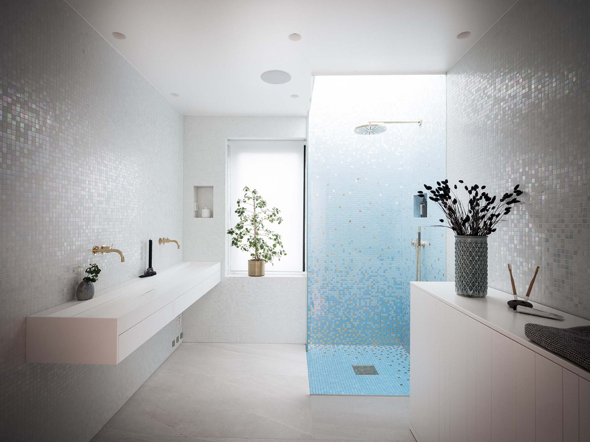 Stiligt - Modernt badrum med vita mosaikplattor, svävande dubbelt handfat, glasdusch med blått klinkergolv, krukväxter och minimalistisk inredning.