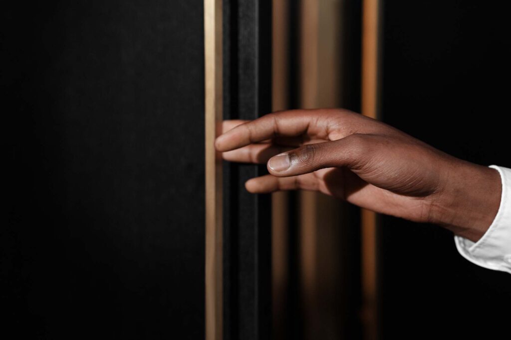 Stiligt - En persons hand, med en ljus skjortmanschett synlig, sträcker sig ut mot en vertikal, guldfärgad kant mot en mörk bakgrund.