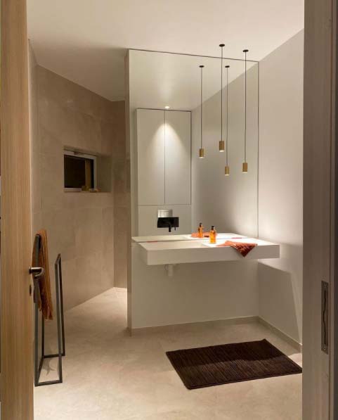 Stiligt - Villa Fernströms badrum Modernt badrum med stor spegel, flytande handfat, stiligt taklampor och beige kakel. En handduk hänger på ett stativ, och toalettartiklar är snyggt arrangerade på bänken.