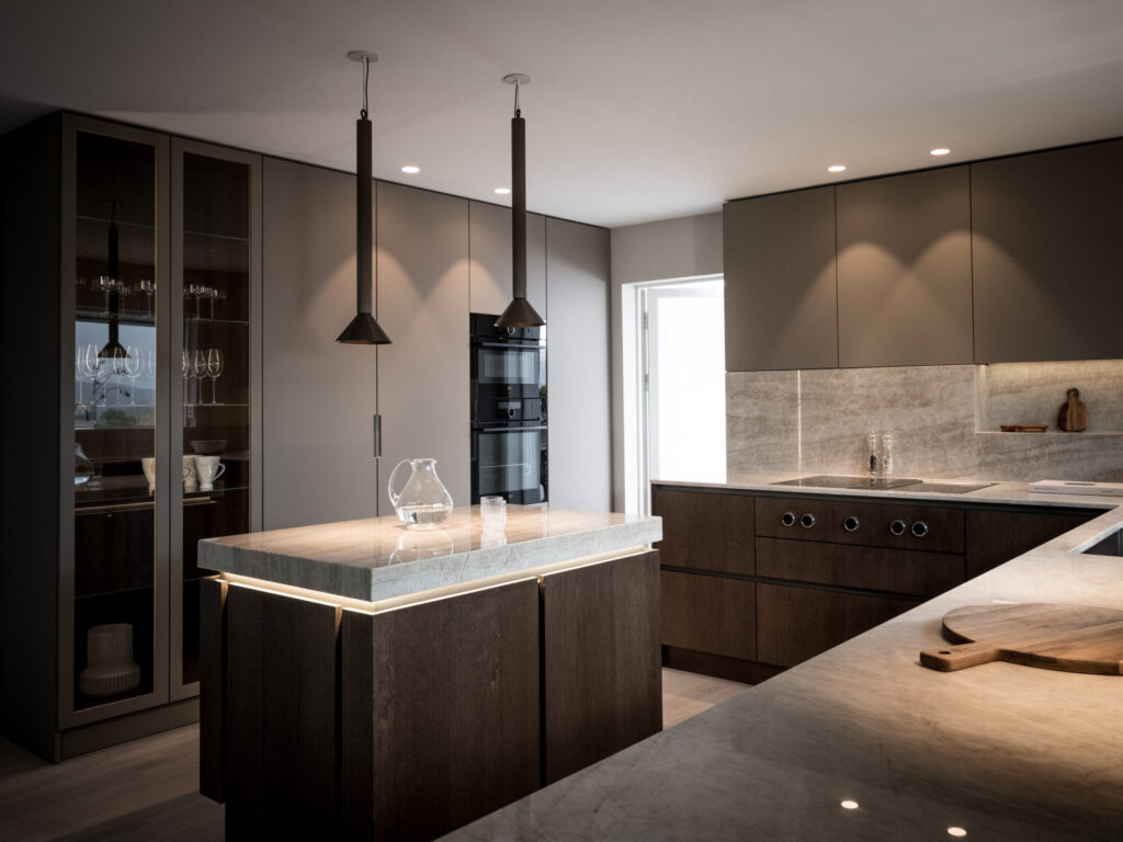 Stiligt - Modernt kök med skåp i mörkt trä, bänkskivor i marmor, pendelbelysning, inbyggda vitvaror och skåp med glasfront som visar glas.