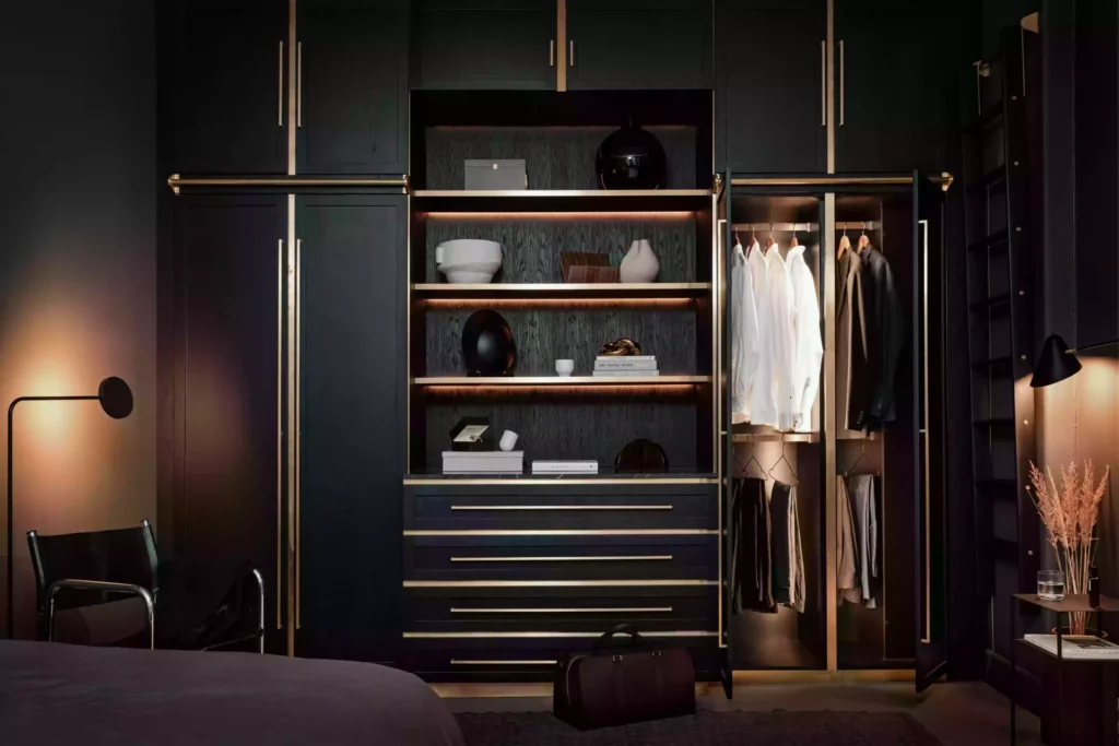 Stiligt - En modern, mörkfärgad Svart Garderob med öppna hyllor visar snyggt arrangerade kläder, lådor, prydnadsföremål och accentbelysning i en stilfull sovrumsmiljö.