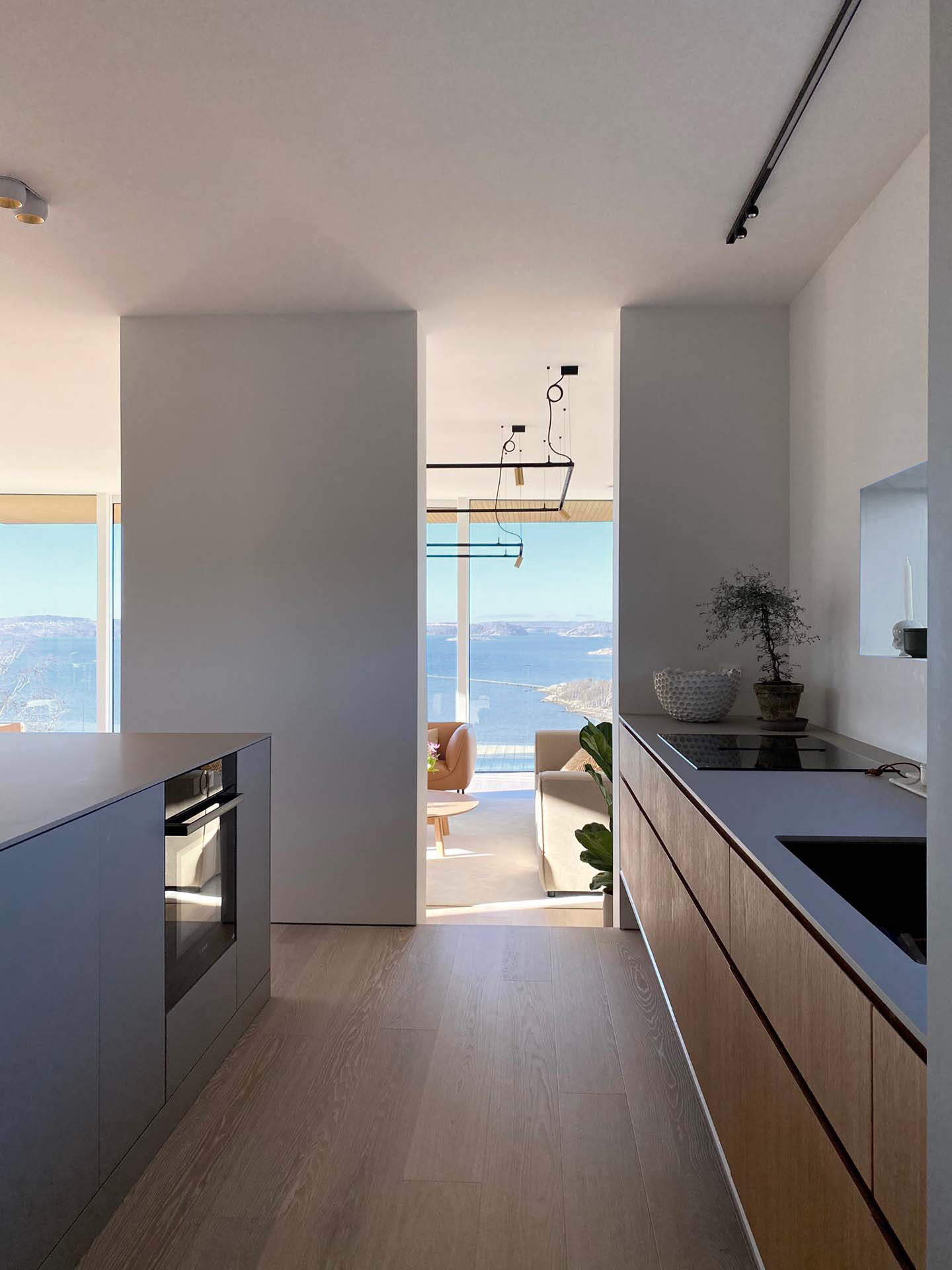 Stiligt - Modernt kök med minimalistisk design öppnar mot ett ljust vardagsrum med stora fönster och utsikt över havet och bergen i bakgrunden.