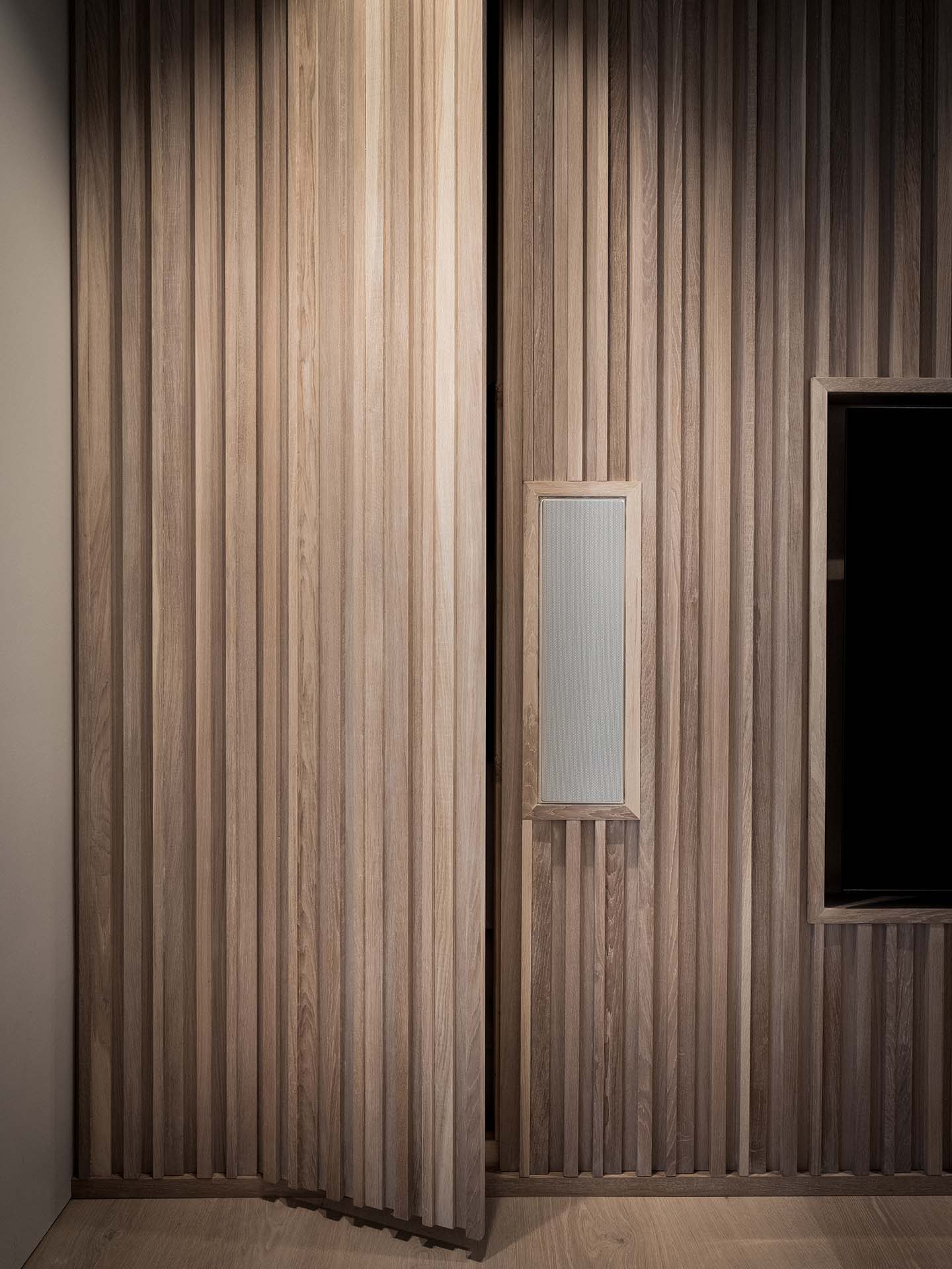 Stiligt - En delvis öppen trädörr med vertikala lameller, intill en vägg med matchande träpanel och en rektangulär infälld panel.