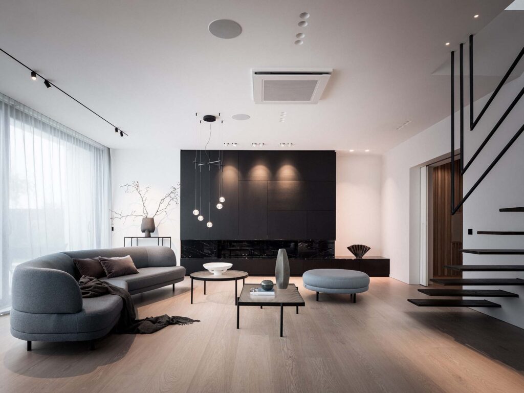 Stiligt - Modernt minimalistiskt vardagsrum med gråa möbler, trägolv, svart accentvägg, flytande trappa och stort fönster med skira gardiner – perfekt för vardagsrumsinspiration.