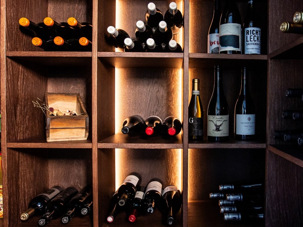 Stiligt - Trähyllor fyllda med diverse vinflaskor, vissa staplade horisontellt och andra stående upprätt, med varm bakgrundsbelysning som framhäver samlingen.