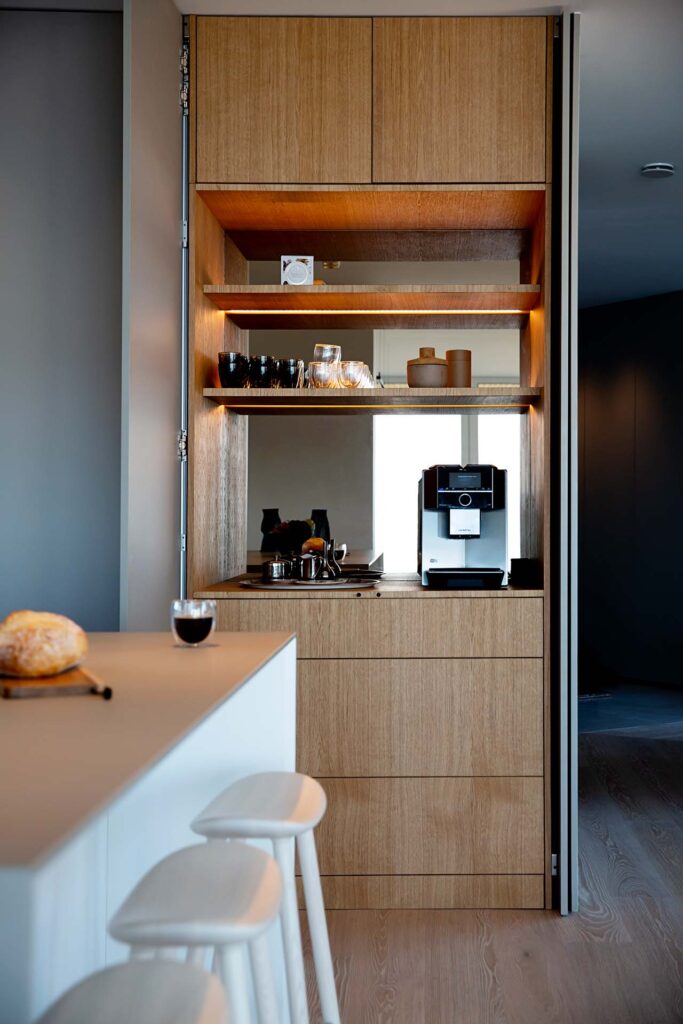 Stiligt - En modern kaffestation i köket med trähyllor med koppar och glas, en kaffemaskin och en bänkskiva med ett glas kaffe och en limpa.