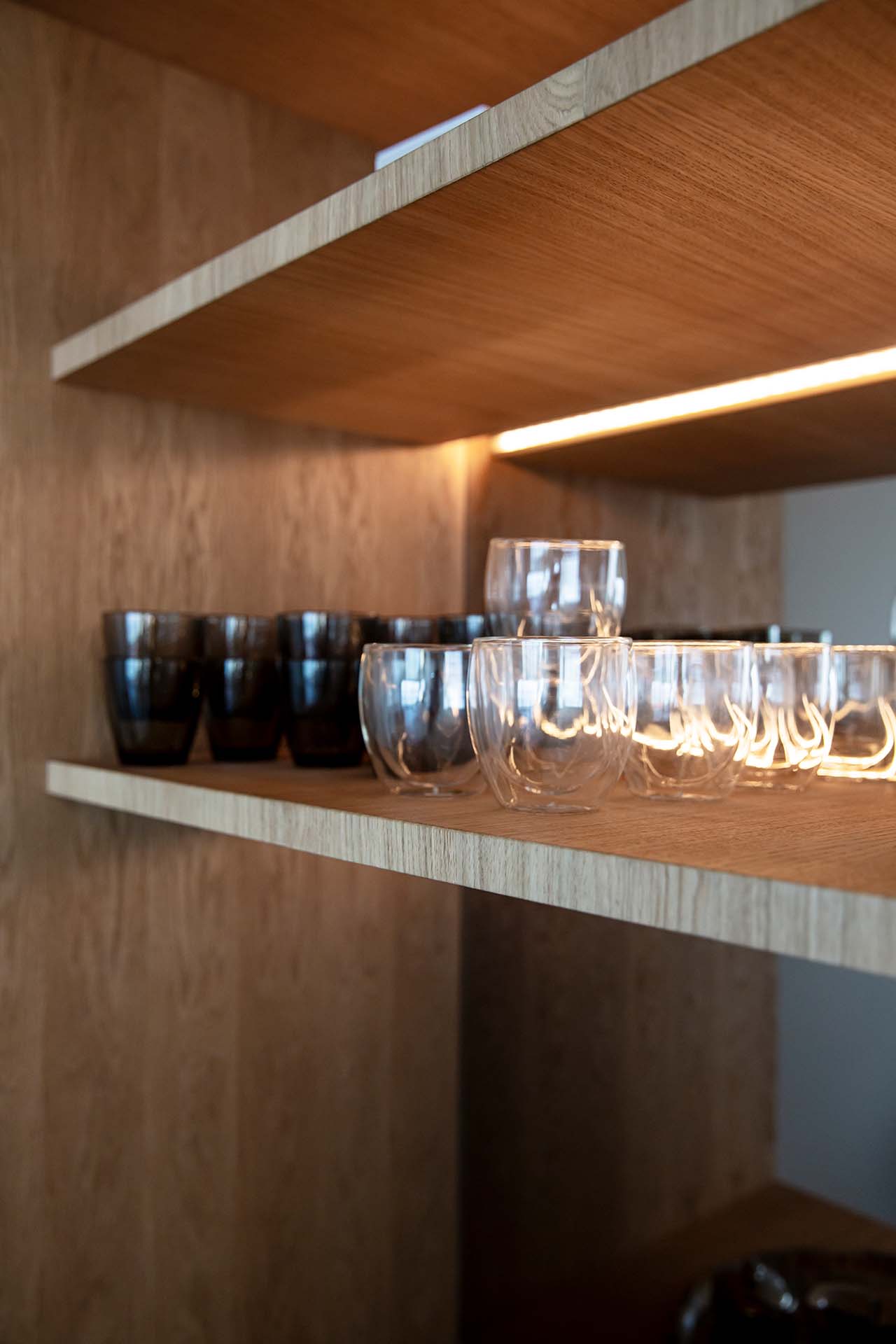 Stiligt - Stiligt trähyllor med prydligt arrangerade glas och mörkfärgade koppar, upplysta av underhylla belysning.