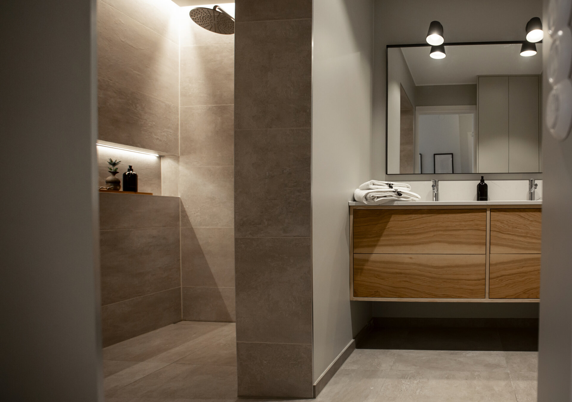 Stiligt - Modernt badrum med duschkabin, beige kakel, ett handfat i trä med dubbla handfat, en stor spegel och minimalistisk belysning.