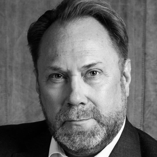 Stiligt - Svartvitt porträtt av en medelålders man med kort hår och skägg, klädd i en kavaj, tittar direkt in i kameran mot en vanlig bakgrund.