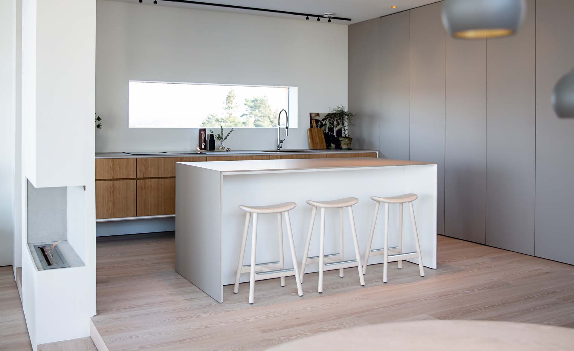 Stiligt - Modernt kök med en vit ö, tre pallar, träskåp och ett stort fönster som ger naturligt ljus. Den neutrala färgpaletten och den minimalistiska designen skapar en stilig atmosfär som blandar elegans med enkelhet.
