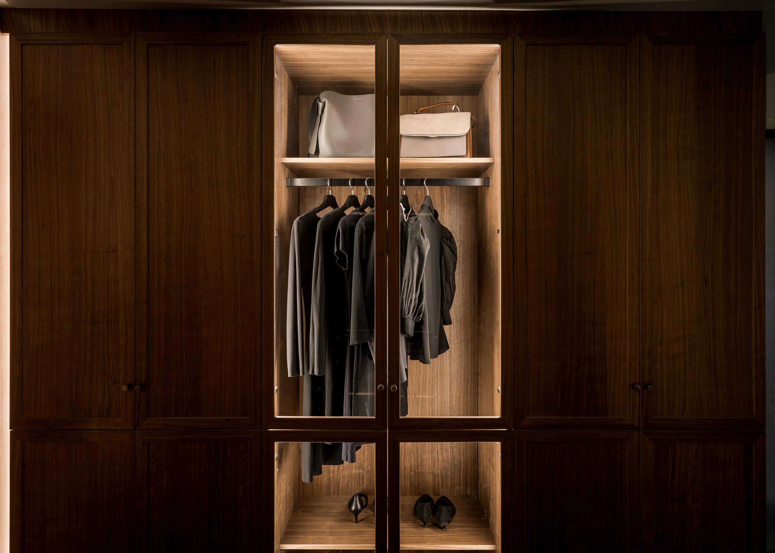 Stiligt - En trägarderob med upplysta hyllor visar snyggt upphängda svarta och gråa kläder, två handväskor på översta hyllan och ett par skor längst ner.