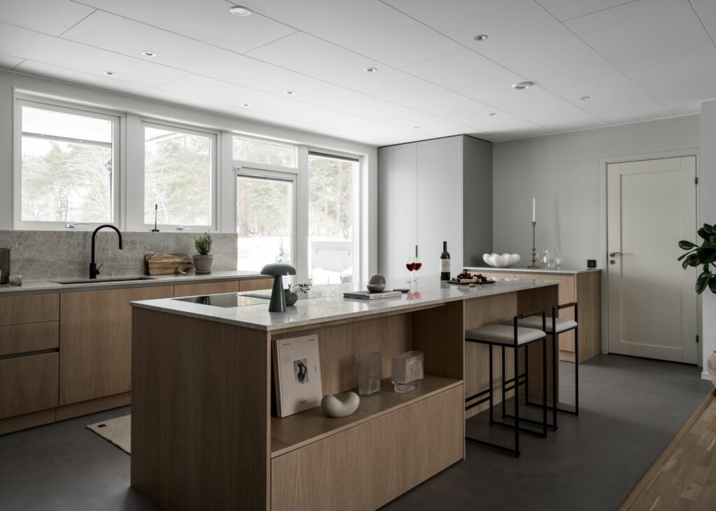 Stiligt - Modernt kök med ljusa träskåp, en marmorö med pallar, inbyggda vitvaror, stora fönster och minimalistisk inredning.